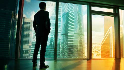 Man in suit in front of a wall of glass overlooking skyscrapers