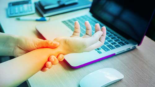 close up of woman holding her wrist in pain in front of a laptop keyboard